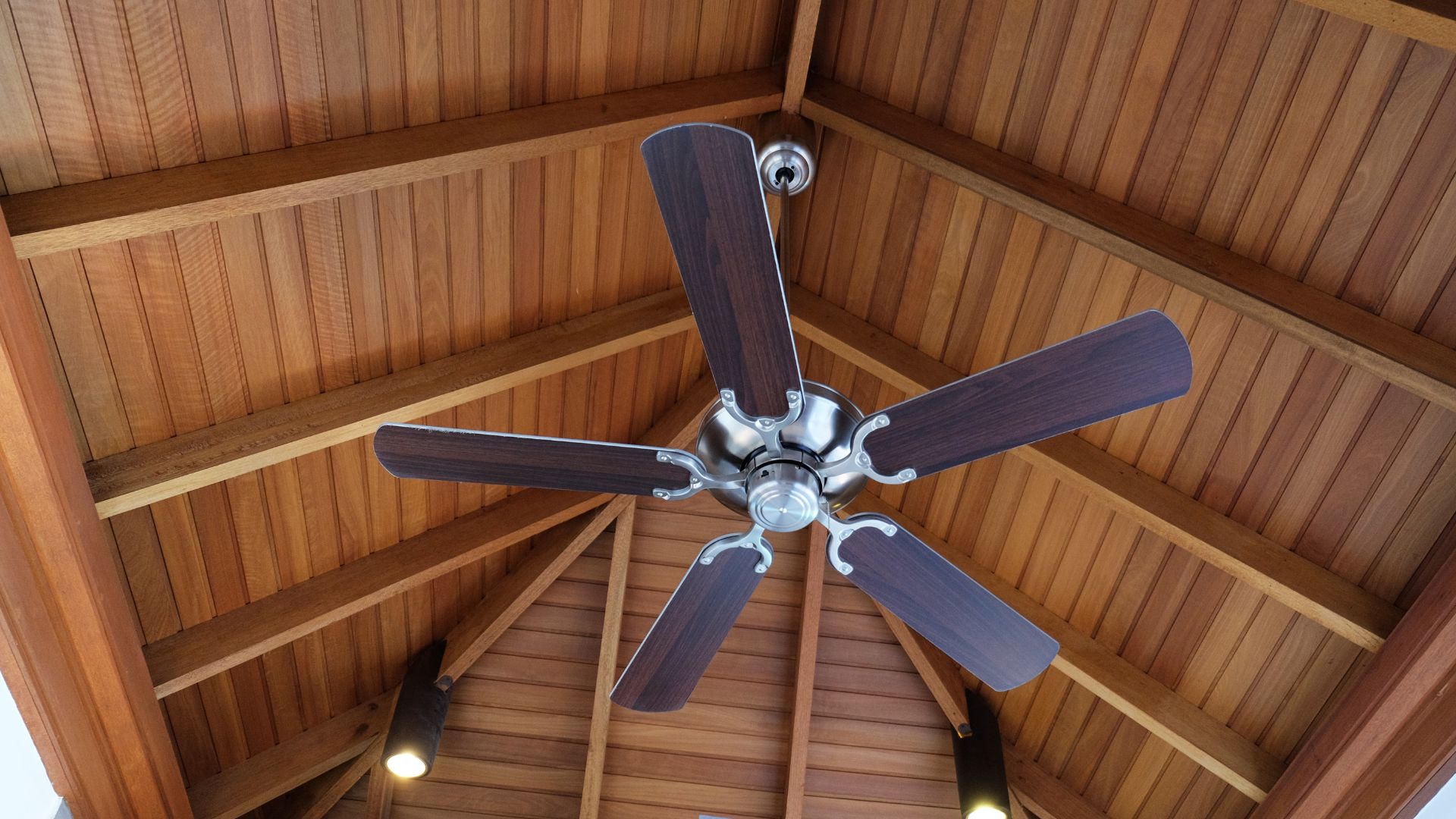 A ceiling fan hanging from a tall wooden ceiling.