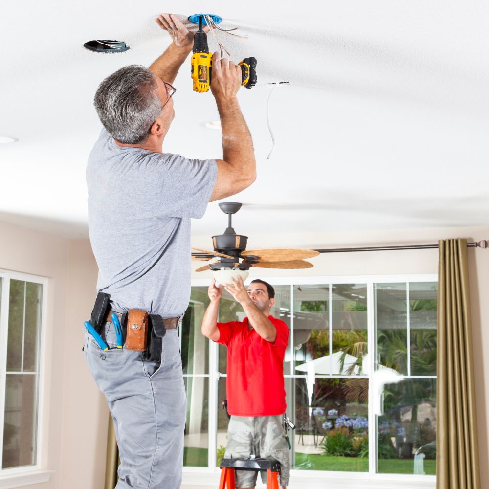 Two electricians installing a ceiling fan.