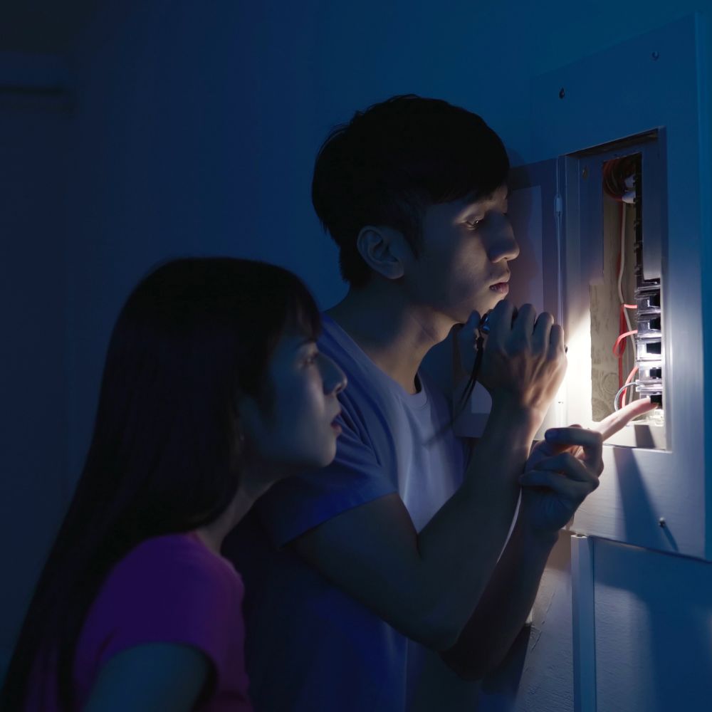 A young couple assessing a breaker box during a power outage.